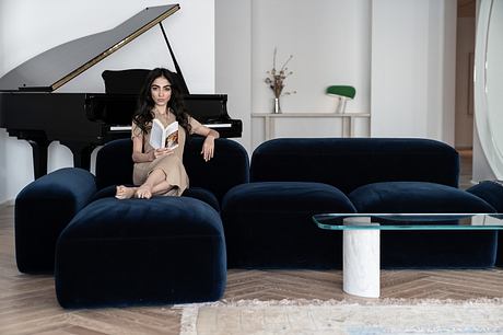 Black grand piano, plush navy sofas, glass-topped table, and a plant decoration against a light wall.