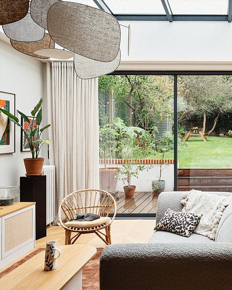 Cozy living room with large windows overlooking a lush garden, featuring modern furniture and natural elements.
