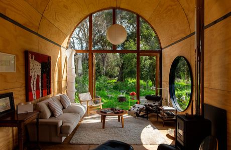 Cozy living room with large arched windows overlooking lush greenery, organic textures.