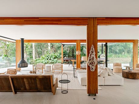 Spacious open-concept living area with warm wooden beams, cozy seating, and lush outdoor views.