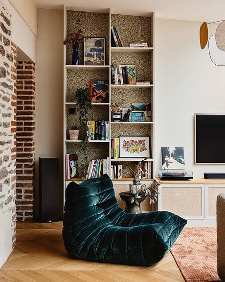 Cozy living room with brick walls, built-in shelves, and a plush green velvet chair.