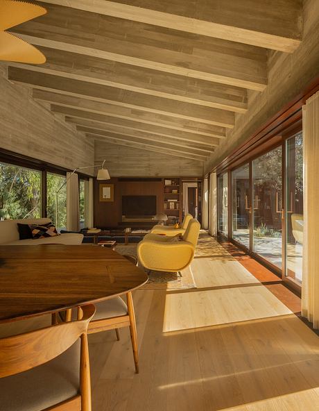 Warm-toned wooden ceiling, expansive windows, and plush yellow furniture create a cozy, modern living space.