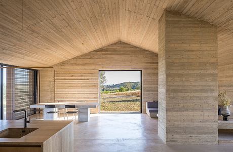 Minimalist interior with vaulted wood ceiling, concrete walls, and panoramic window view.