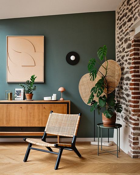 Cozy living room with wooden furniture, geometric decor, and lush greenery against brick walls.