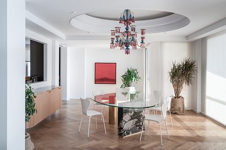 A bright, modern dining room with a glass table, chandelier, and wood-paneled walls.