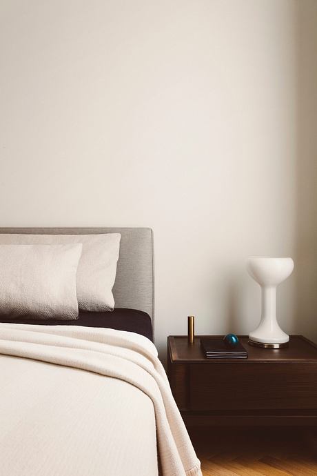 Minimalist bedroom with neutral colors, wooden nightstand, and decorative lamp.