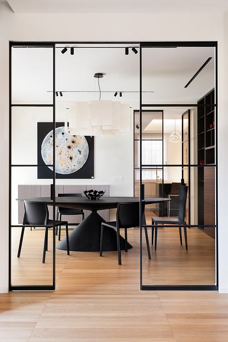 Minimalist dining room with sleek black-framed glass walls, modern furnishings, and artistic decor.
