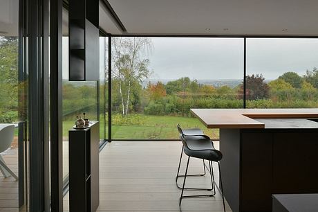 Sleek modern kitchen overlooking lush green landscape through vast glass walls.
