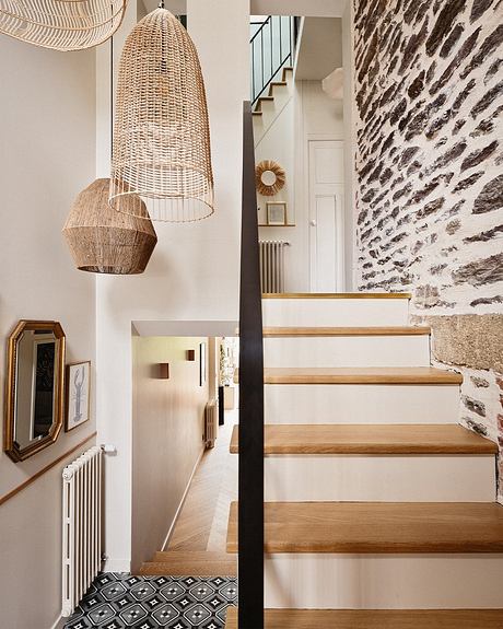 An inviting entryway with textured stone walls, wooden staircase, and modern pendant lamps.