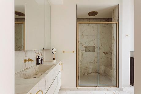 Spacious marble-clad bathroom with minimalist vanity, brass fixtures, and glass shower.