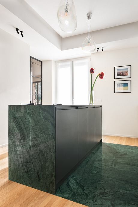 Sleek, modern kitchen with glossy green marble island, pendant lighting, and artwork.