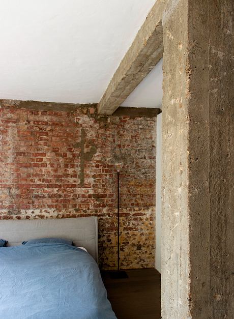 Rustic bedroom with exposed brick walls and concrete ceiling beams, creating a cozy, industrial ambiance.