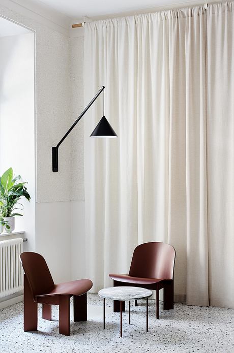 Minimalist living room with a black wall sconce, maroon chairs, and a marble-topped table.