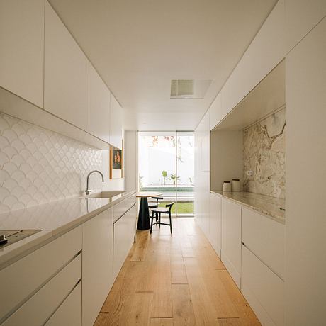 Sleek, minimalist kitchen with white cabinets, wood floors, and a view to the outdoors.
