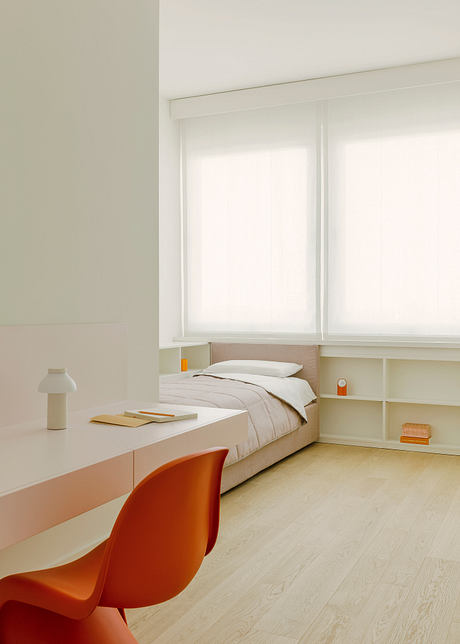 Minimalist bedroom with white walls, built-in storage, and an orange accent chair.