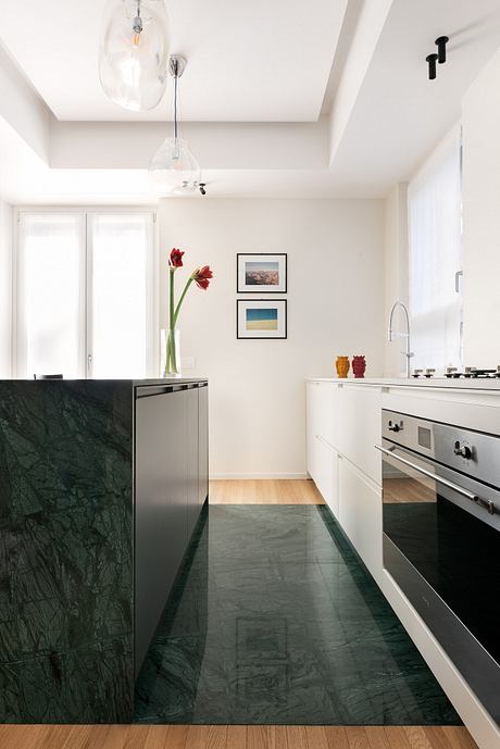 A modern kitchen with a sleek black marble countertop, white cabinetry, and minimalist lighting.