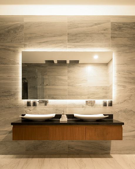 Modern bathroom design with stone tile walls, wooden vanity, dual sinks, and backlit mirror.