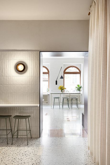 A modern, minimalist kitchen with sleek white cabinetry, arched windows, and terrazzo floors.