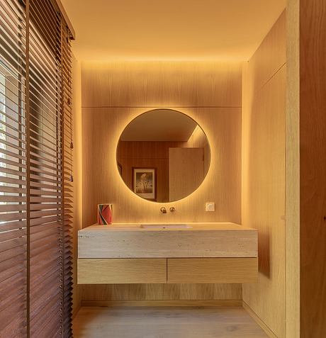 Modern vanity with circular mirror, stone countertop, and warm wood tones in bathroom.