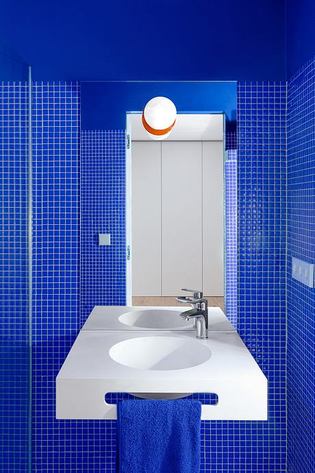 A modern bathroom with bright blue tile walls, a white vanity, and a circular light fixture.