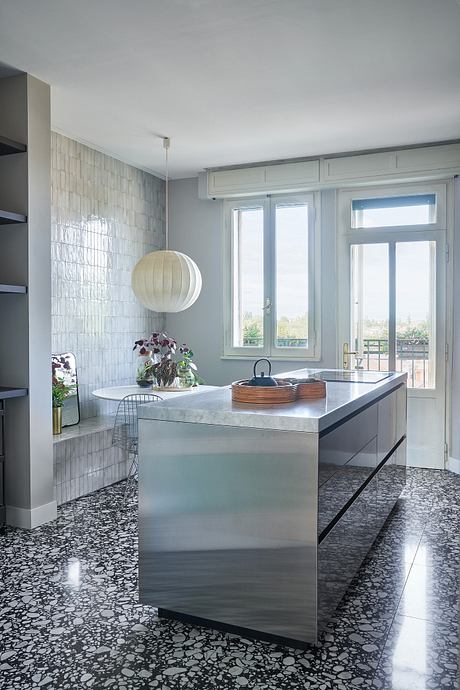 A sleek, modern kitchen with stainless steel countertops, tiled walls, and a white pendant light.
