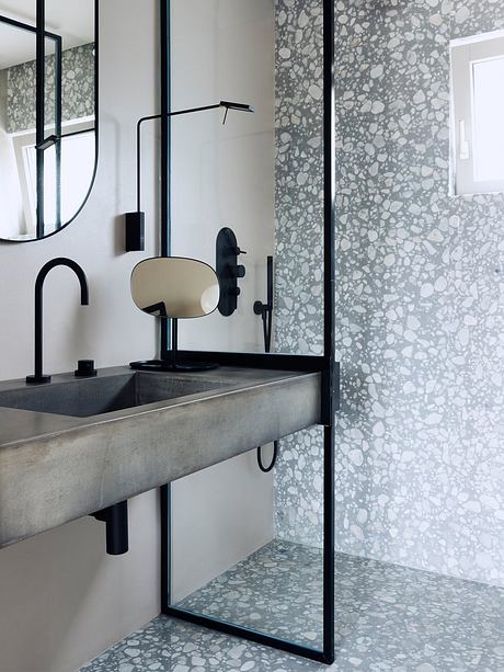 A modern bathroom with a concrete sink, black fixtures, and patterned tile walls.