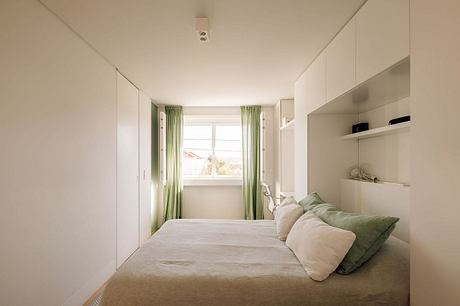 A cozy, minimalist bedroom with white walls, green curtains, and built-in storage.