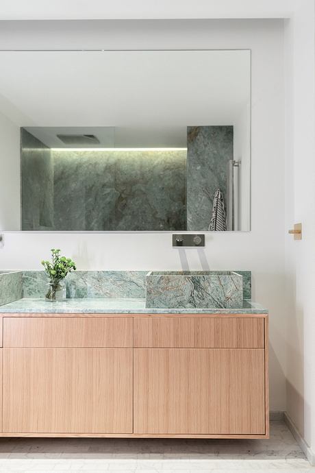 A modern bathroom with a green marble sink and vanity, subtle lighting, and a large mirror.