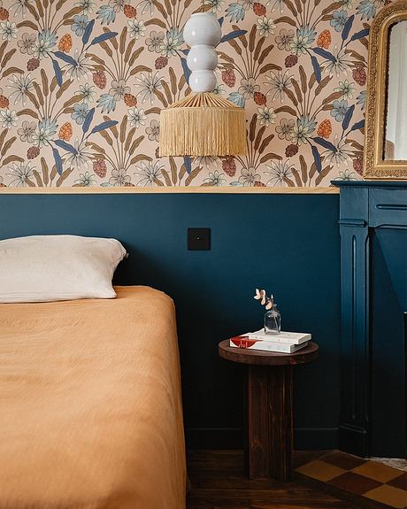 Vibrant floral wallpaper, rattan lighting, and rich, dark accents create a cozy, stylish bedroom.