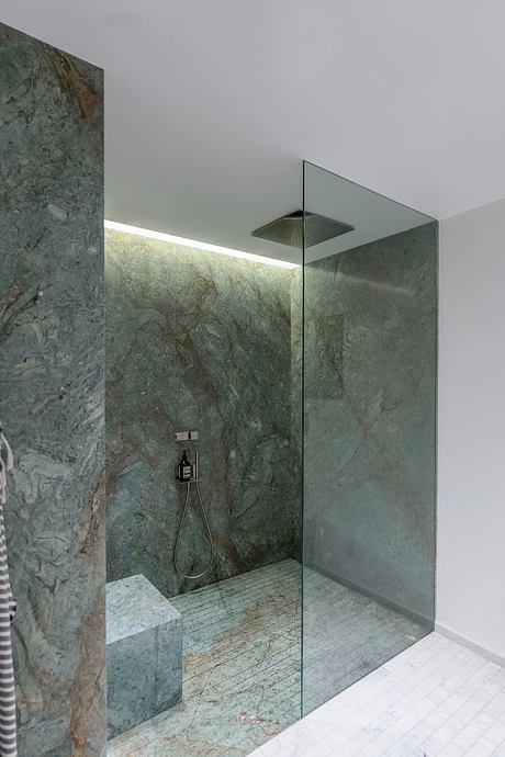 A modern, minimalist bathroom with floor-to-ceiling glass walls and a marble-clad shower.