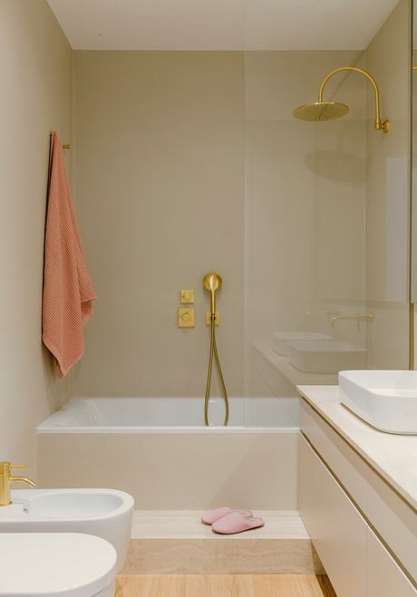 Minimalist bathroom with gold fixtures, white vanity, and a pink towel.