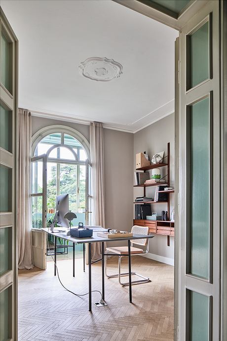 Elegant home office with arched windows, parquet floors, and built-in shelving.