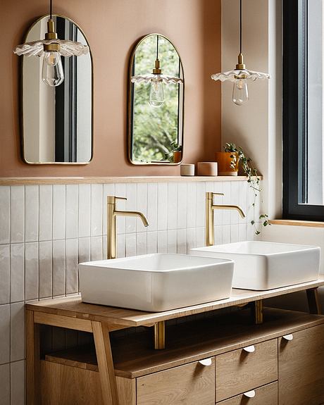 Elegant bathroom with white vessel sinks, gold faucets, arched mirrors, and pendant lights.