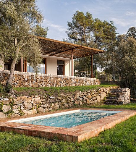 Rustic stone walls, wooden pergola, and a tranquil swimming pool nestled in a lush, wooded setting.