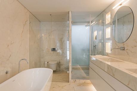 Spacious modern bathroom with marble walls, freestanding tub, and glass-enclosed shower.