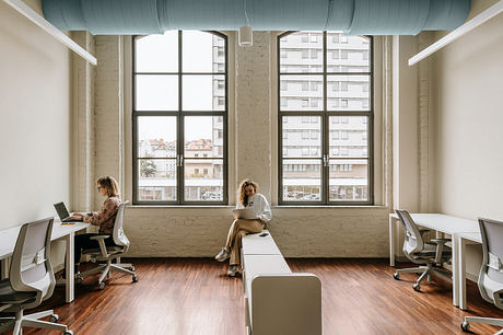 Large windows flood the modern office with natural light, accentuating the minimalist design.