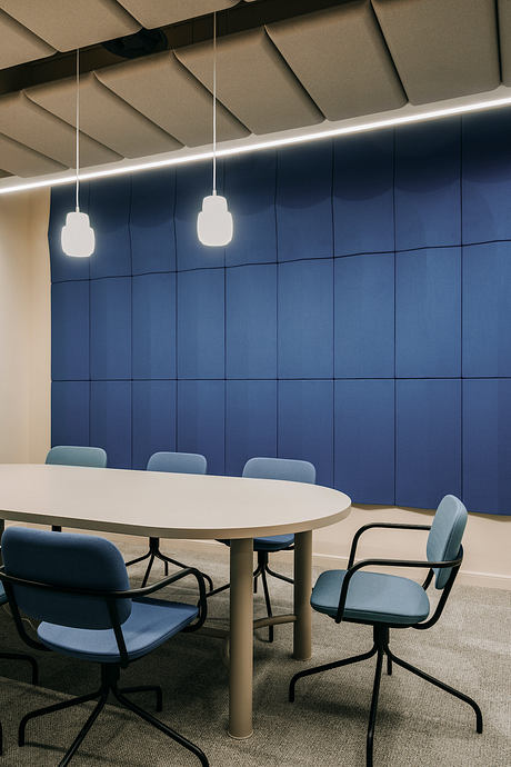 Modern meeting room with white table, blue upholstered chairs, and geometric ceiling design.