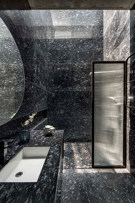 A sleek, modern bathroom with dark marble walls, a minimalist sink, and frosted glass details.