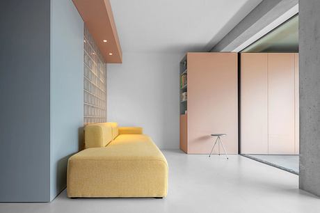 Minimalist living room with yellow sofa, built-in storage, and concrete walls.