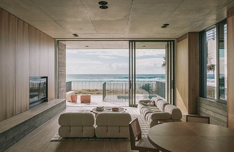 A spacious living room with floor-to-ceiling windows overlooking the ocean, featuring a modern, minimalist design.