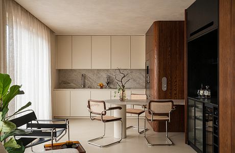 Minimalist kitchen with wood cabinetry, marble backsplash, and modernist dining chairs.