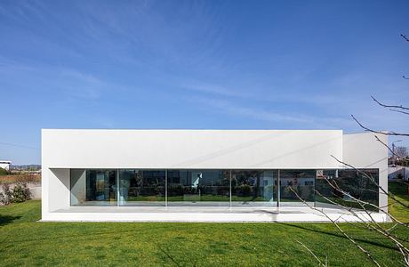 A minimalist, modern building with clean lines, large glass windows, and a grassy lawn.