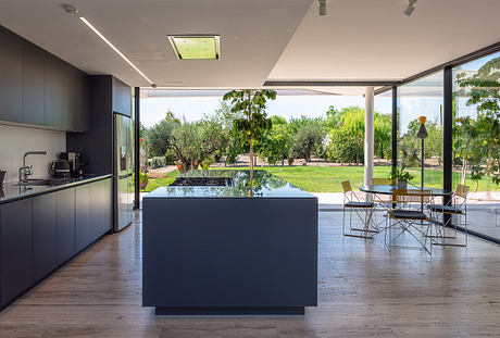 Modern, open-concept kitchen and dining area with sleek black island, reflecting pool, and lush outdoor views.
