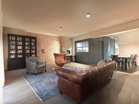 Spacious loft-style living room with exposed brick walls, leather sofa, and library.
