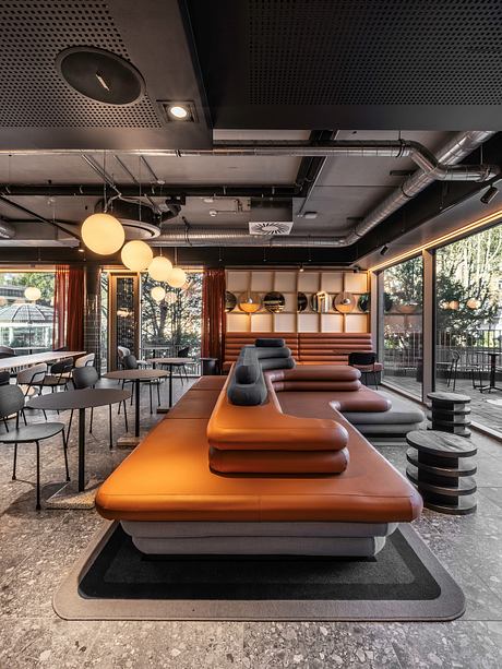 Sleek modern lounge with orange leather seating, pendant lights, and industrial ceiling.