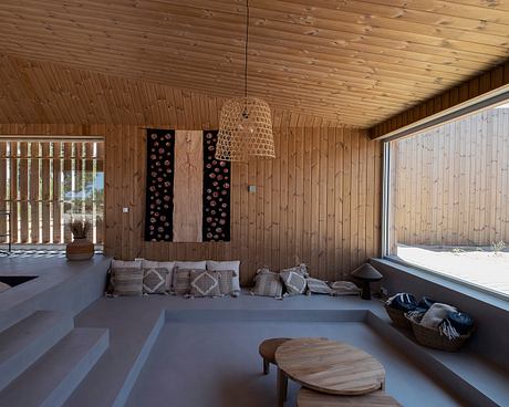 A cozy interior with wooden walls and ceiling, a woven pendant lamp, and a sunken seating area.