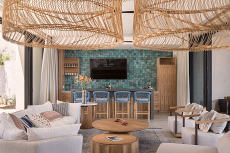 A cozy tropical-inspired lounge with woven rattan pendants, teal mosaic tiles, and wooden furnishings.
