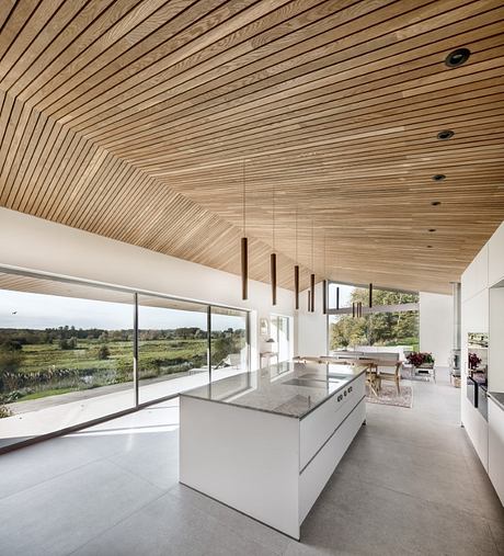 Expansive wooden ceiling supported by evenly spaced beams, complementing the modern kitchen and surrounding nature.