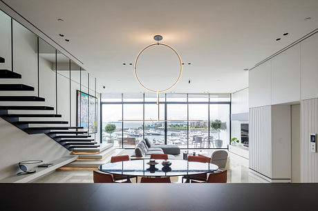 Sleek, modern living space with stunning floor-to-ceiling windows, dramatic staircase, and stylish furnishings.