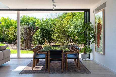 A modern dining area with wood furniture and a lush garden view through large windows.